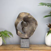 Abstract metal sculpture on a wooden surface with plants in the background